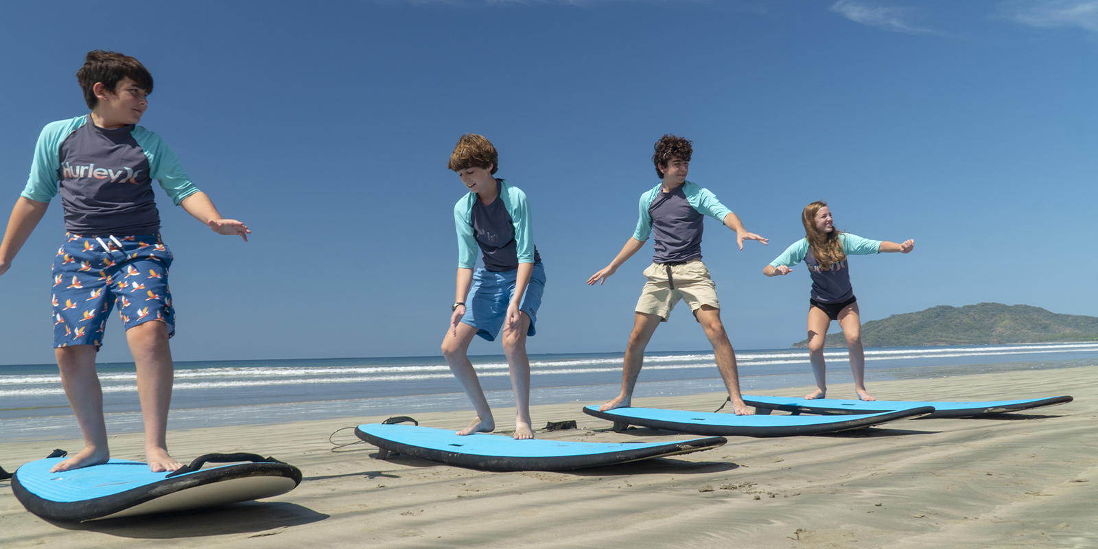 four children practicing surfing on the sand