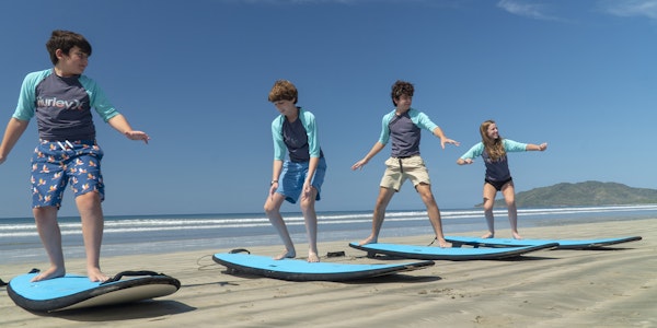 four children practicing surfing on the sand