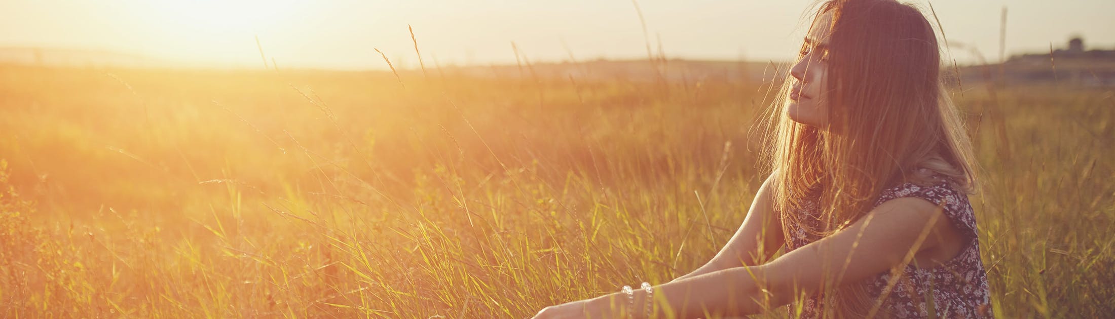 Woman sitting in a field at sunset