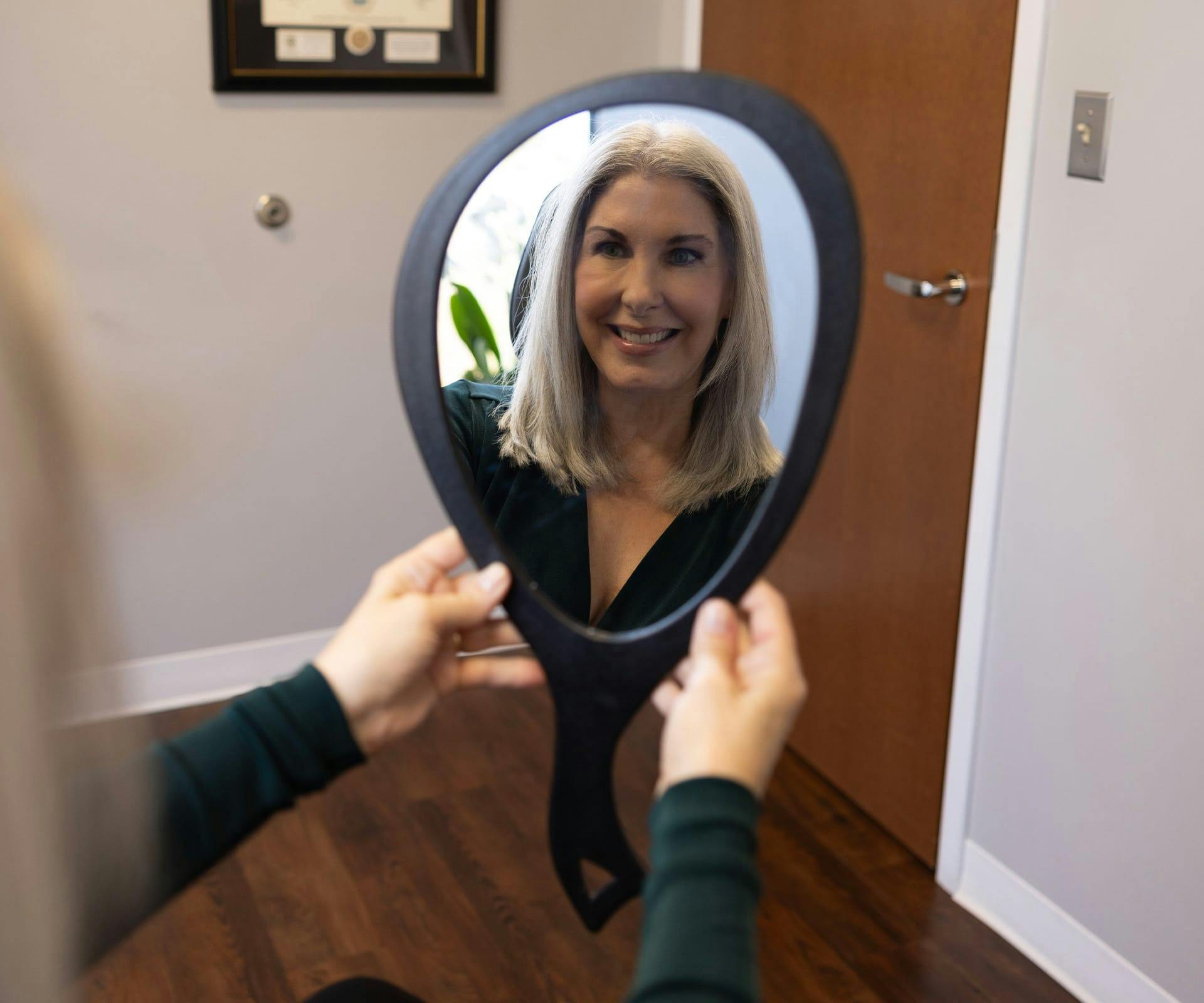 Woman smiling into hand mirror