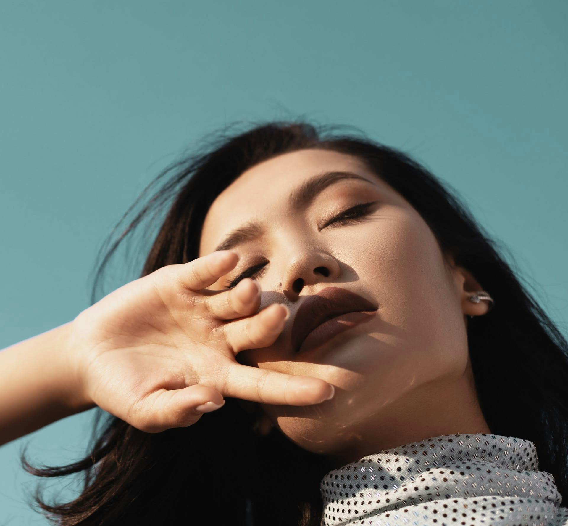 glamorous woman outside with her eyes closed and hand over her face