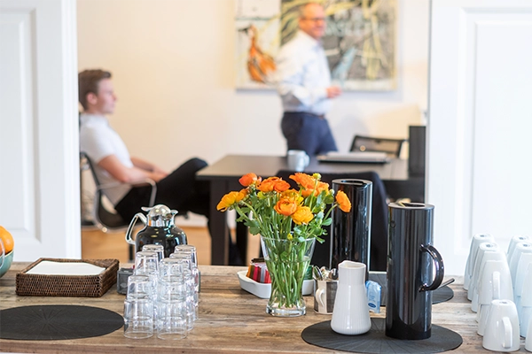 Nærbillede af kaffebord hos Compass, i baggrunden kan man ane to mænd i undervisningslokalet