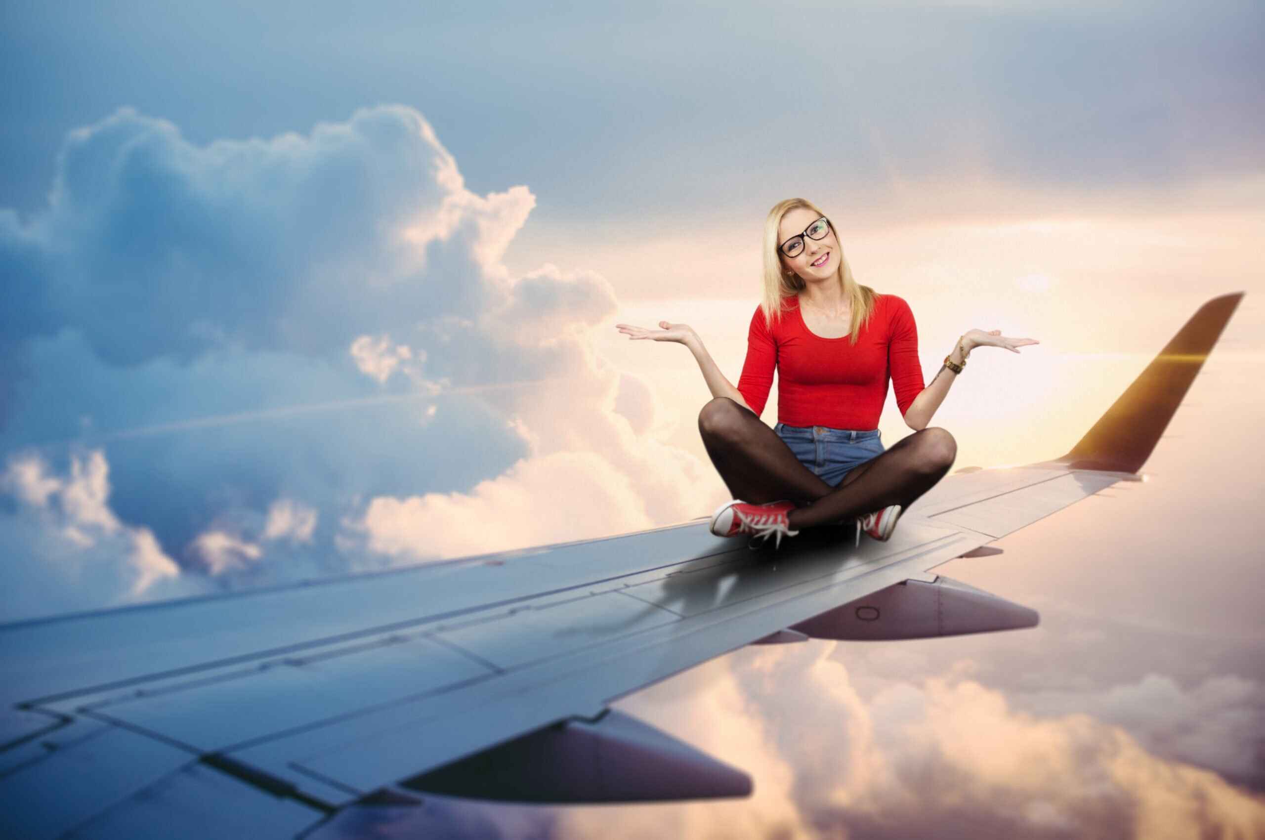 En ung kvinde som sidder i skrædderstilling, er blevet photoshoppet ind på et flys vinge, mens flyet flyver i luften