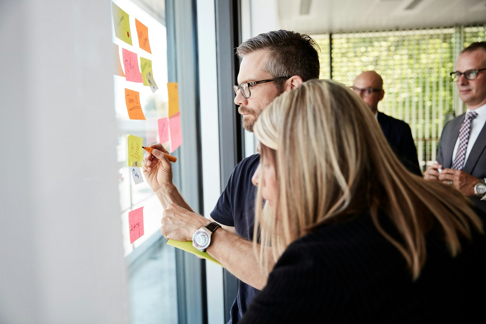 People writing on sticky notes placed on a clear surface during a collaborative work session.