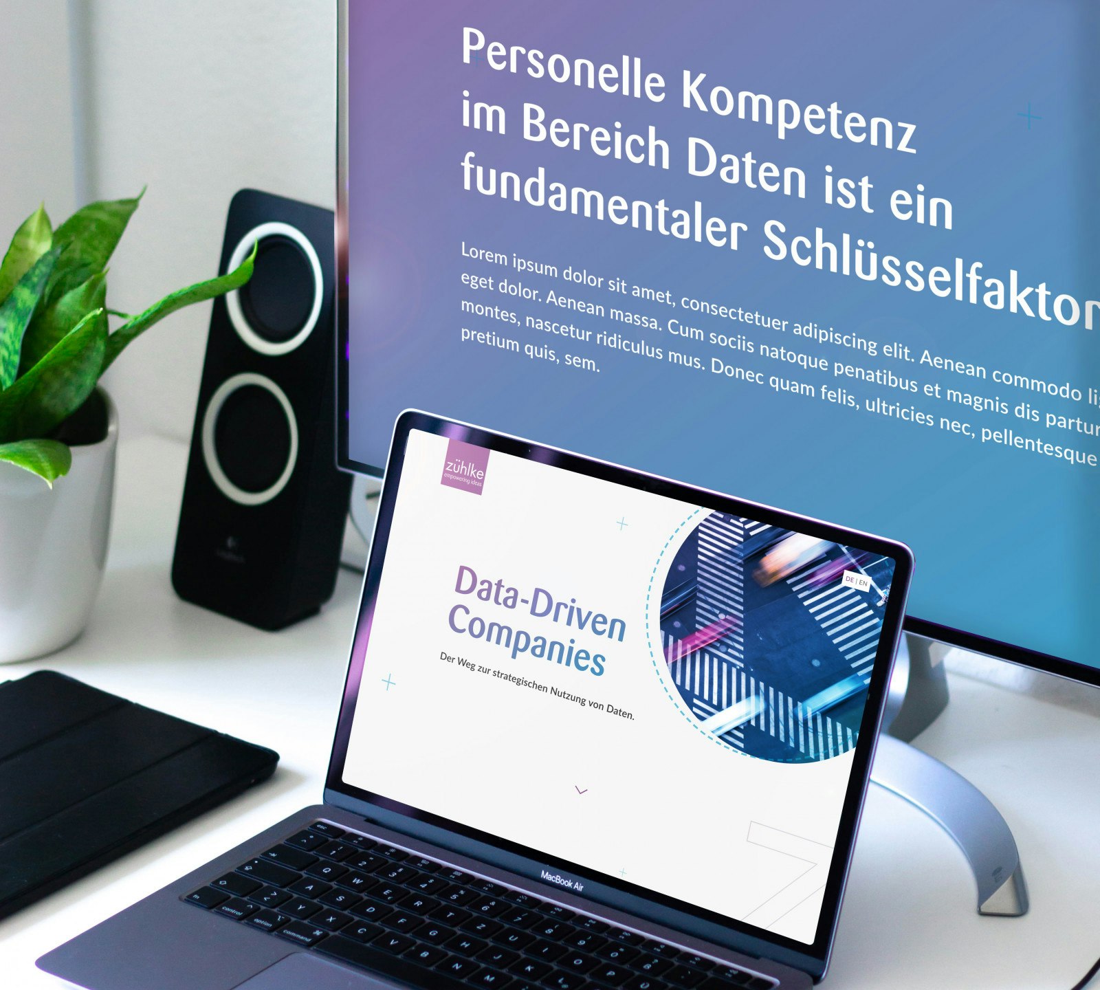 Close-up of a laptop and monitor displaying presentations about data-driven companies. A potted plant and speakers are in the background.