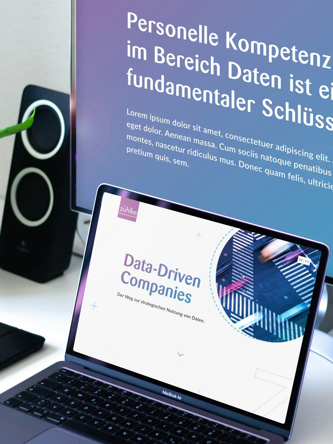 Close-up of a laptop and monitor displaying presentations about data-driven companies. A potted plant and speakers are in the background.