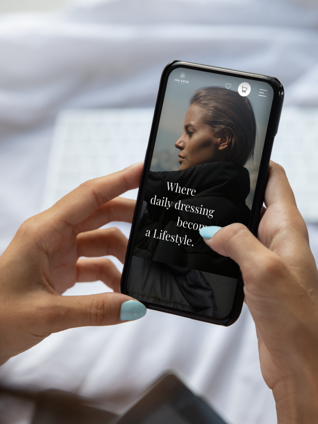 A person holding a smartphone with an on-screen fashion ad that reads, "Where daily dressing becomes a Lifestyle," in front of a blurred keyboard background.