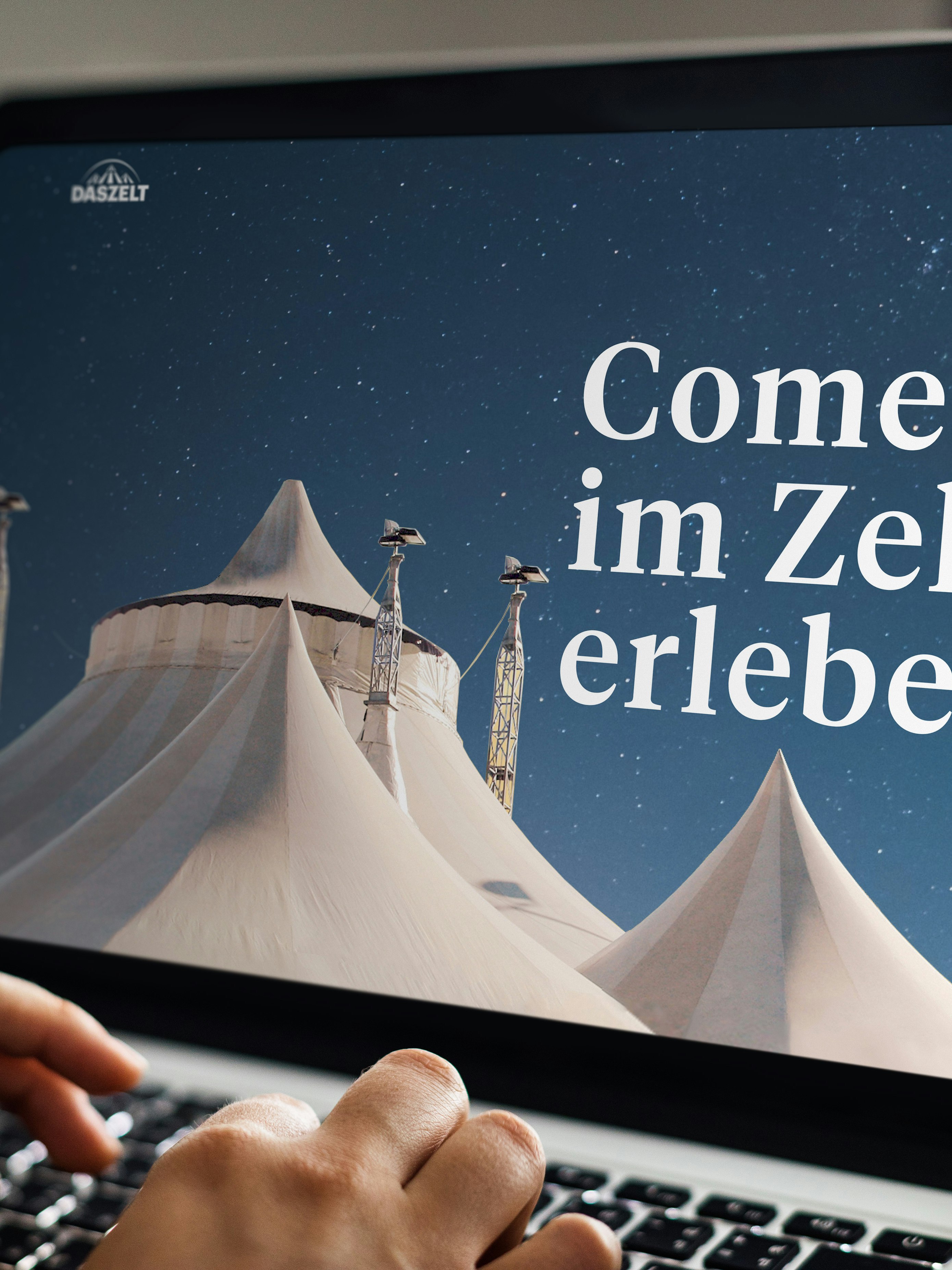 A person types on a laptop displaying a webpage with white tents under a starry sky. The text reads "Comedy im Zelt erleben.