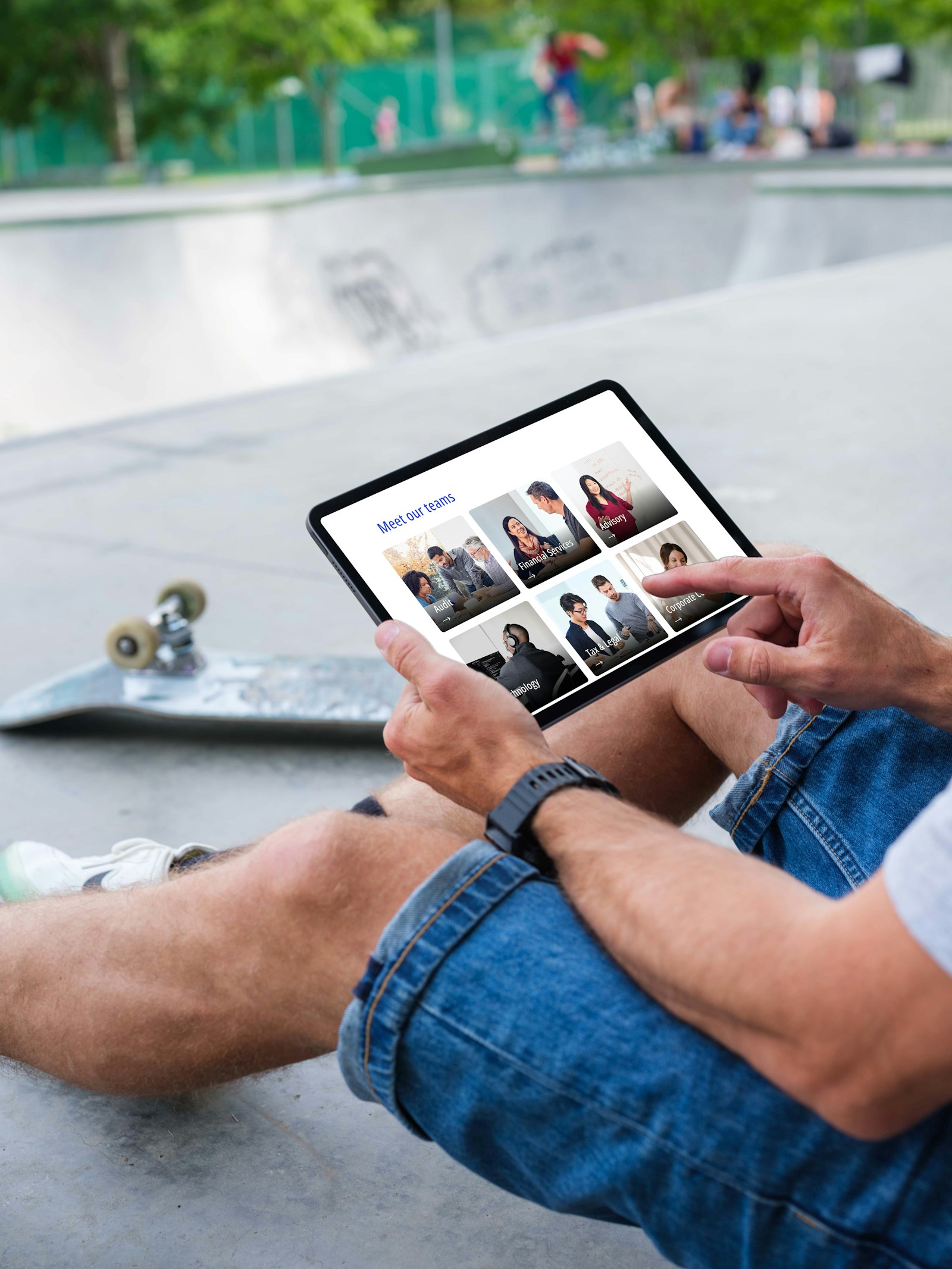 A person sitting by a skateboard looks at a tablet displaying a gallery of six people labeled "Meet our team.