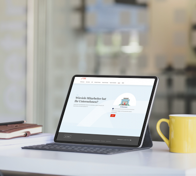 Tablet on a table displaying a website with a question about company employees. A keyboard case, a stack of books, and a yellow mug are also on the table.