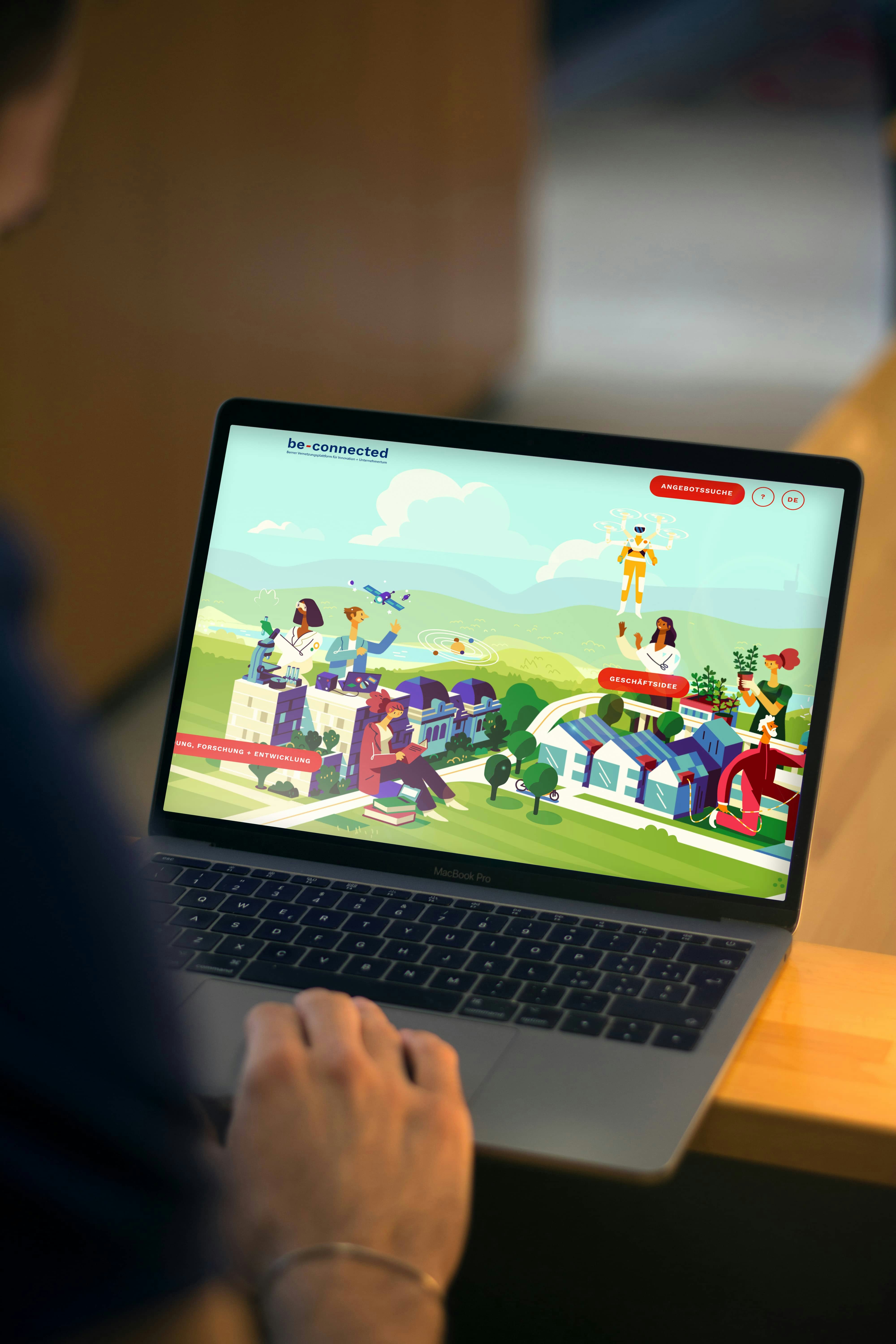 Person using a laptop displaying a webpage with colorful illustrations of people, buildings, and nature, featuring "be-connected" at the top.