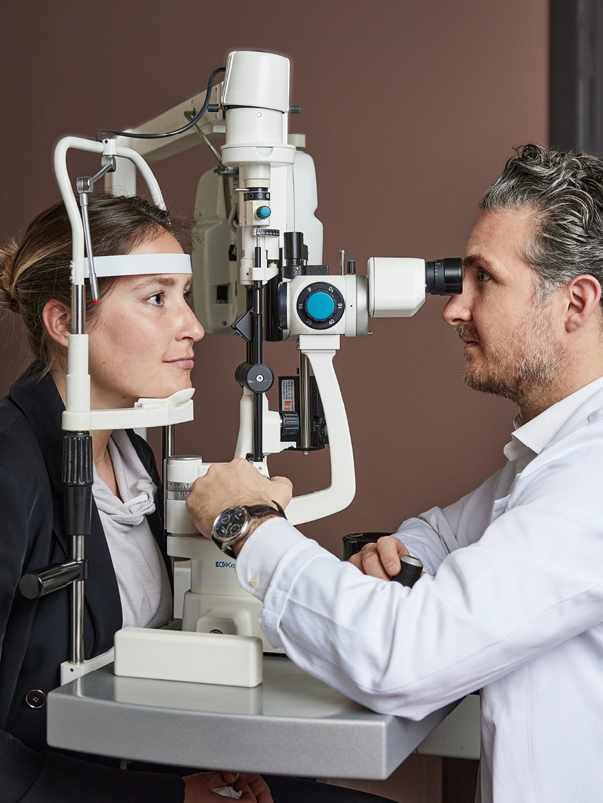 An eye doctor conducts an eye examination on a patient using a slit lamp in a clinic.
