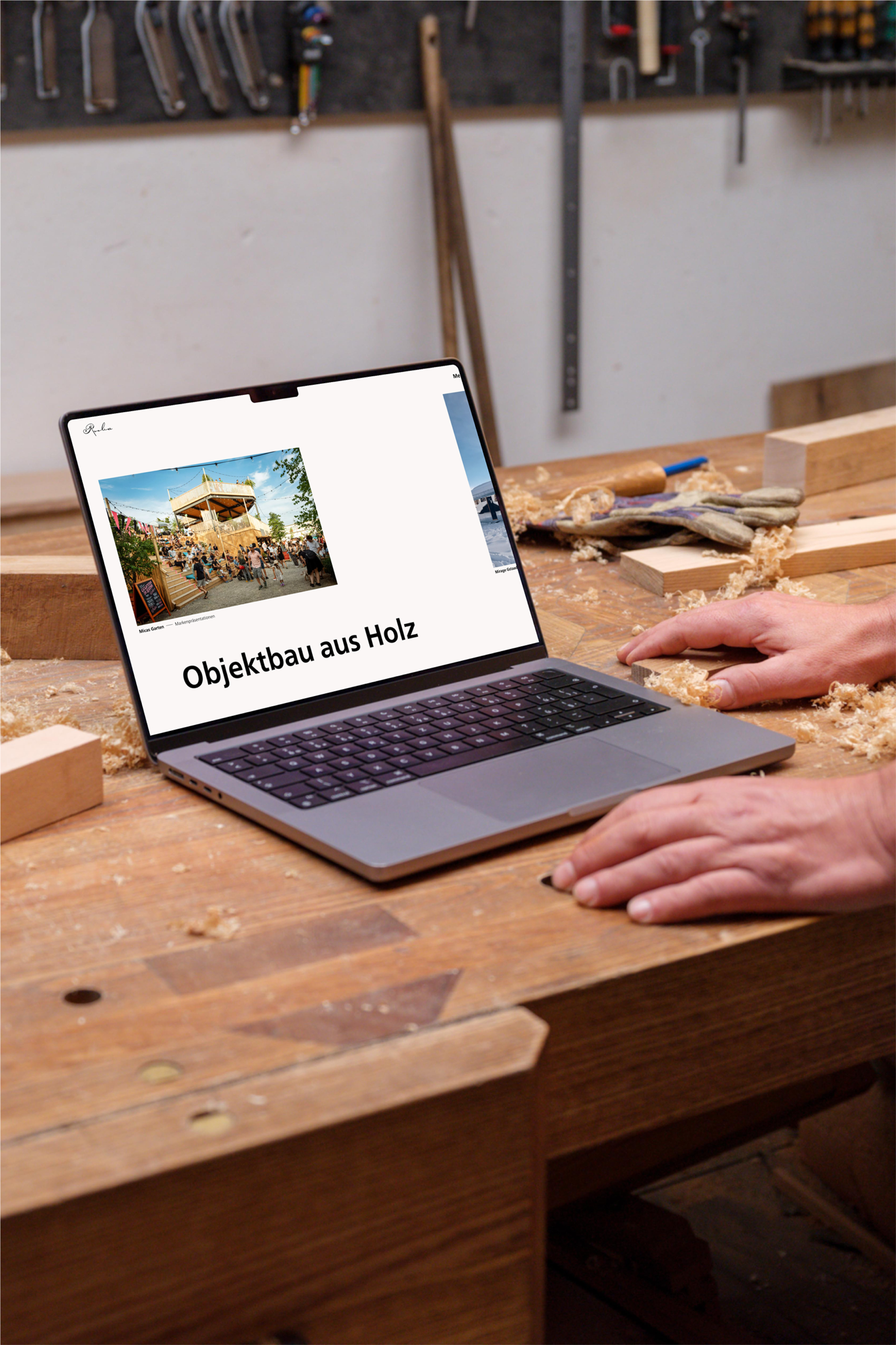 A person works at a wooden workbench with a laptop showing "Objektbau aus Holz," surrounded by wood shavings and tools.
