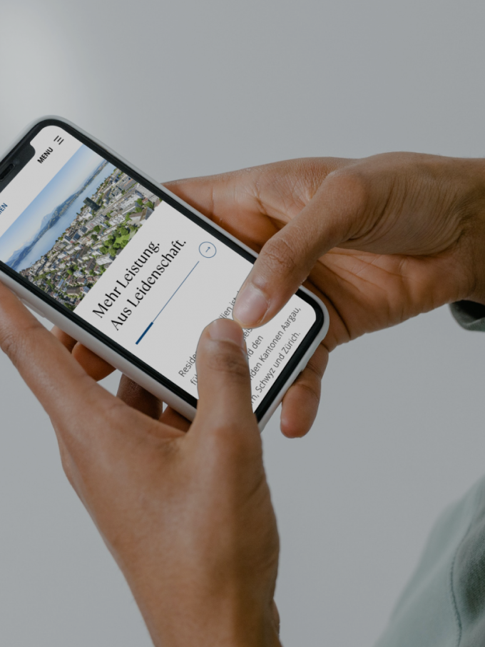 A person holds a smartphone displaying a webpage titled "More Learning, Less Judgement." The screen shows a photo of a landscape and text. The phone is held with both hands against a gray background.