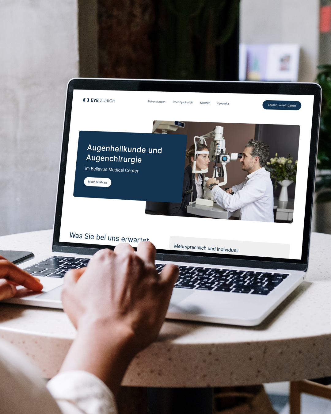 Person using a laptop displaying a website with an eye examination scene and text in German related to ophthalmology and eye surgery.