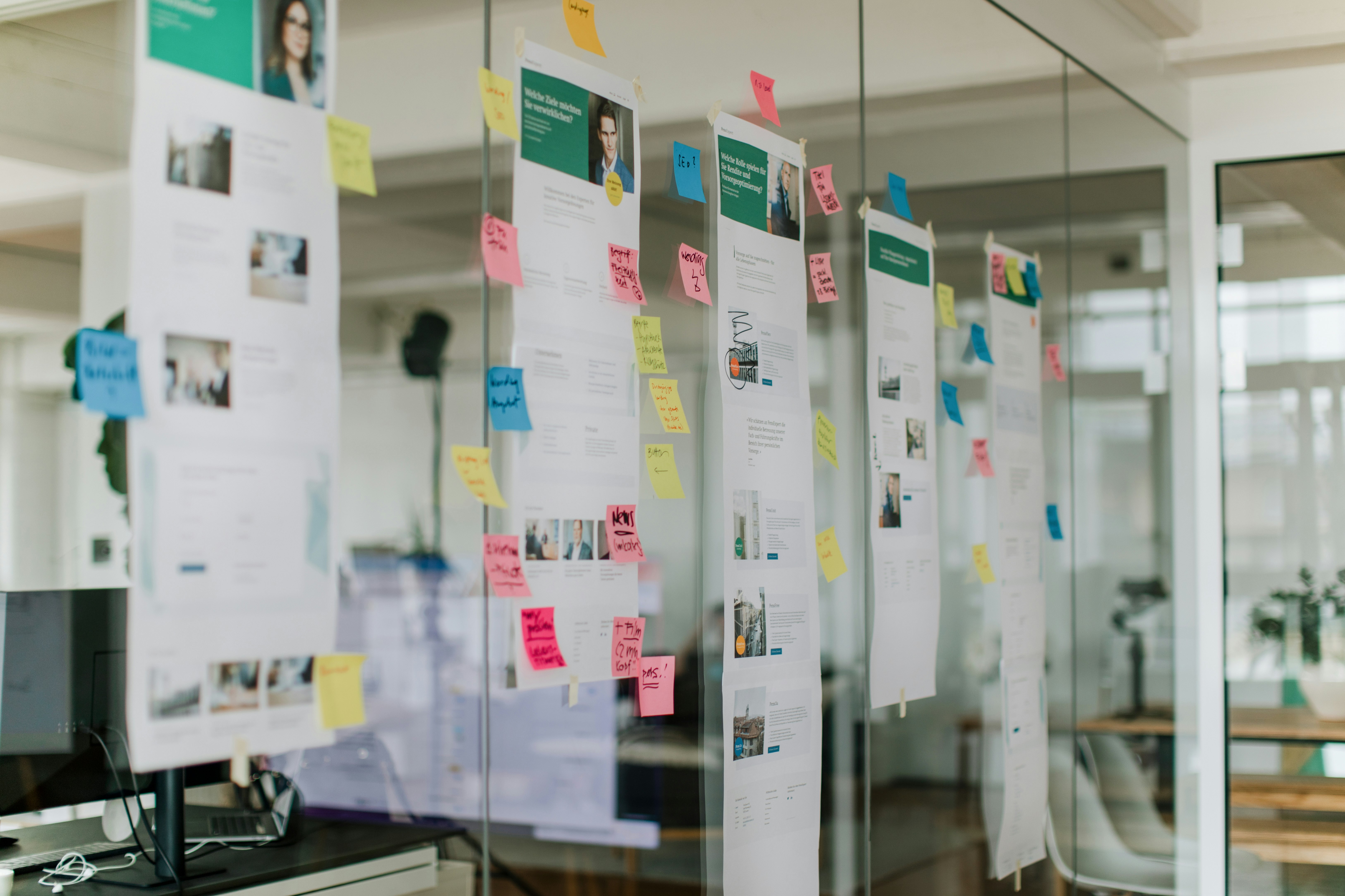 Sections of a website are attached to a glass wall with colorful sticky notes.