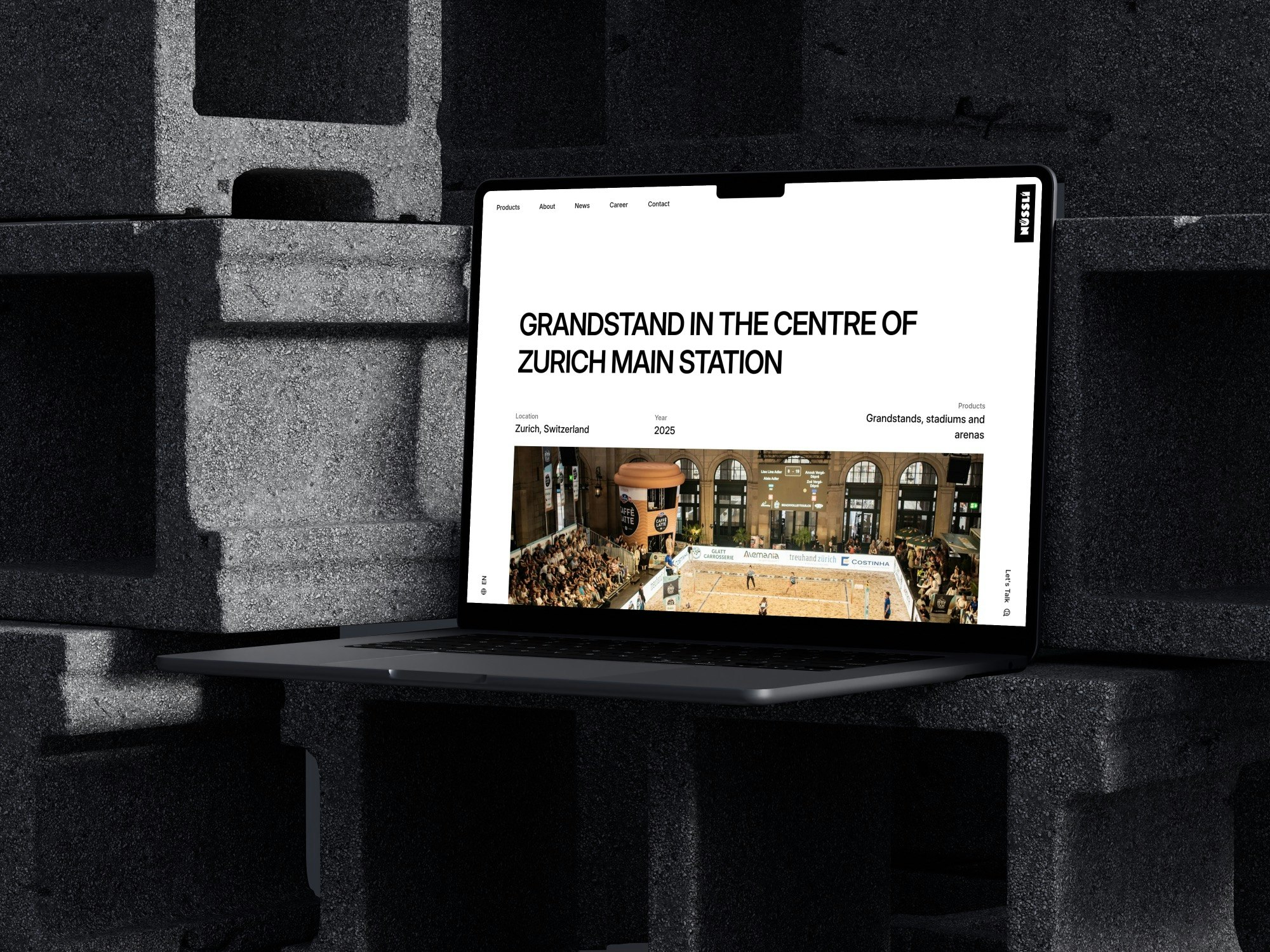 Ein Laptop ruht auf gestapelten Betonblöcken und zeigt eine Website mit der Überschrift Tribüne im Zentrum des Zürcher Hauptbahnhofs über einem Foto einer Sportveranstaltung in einer großen Halle.