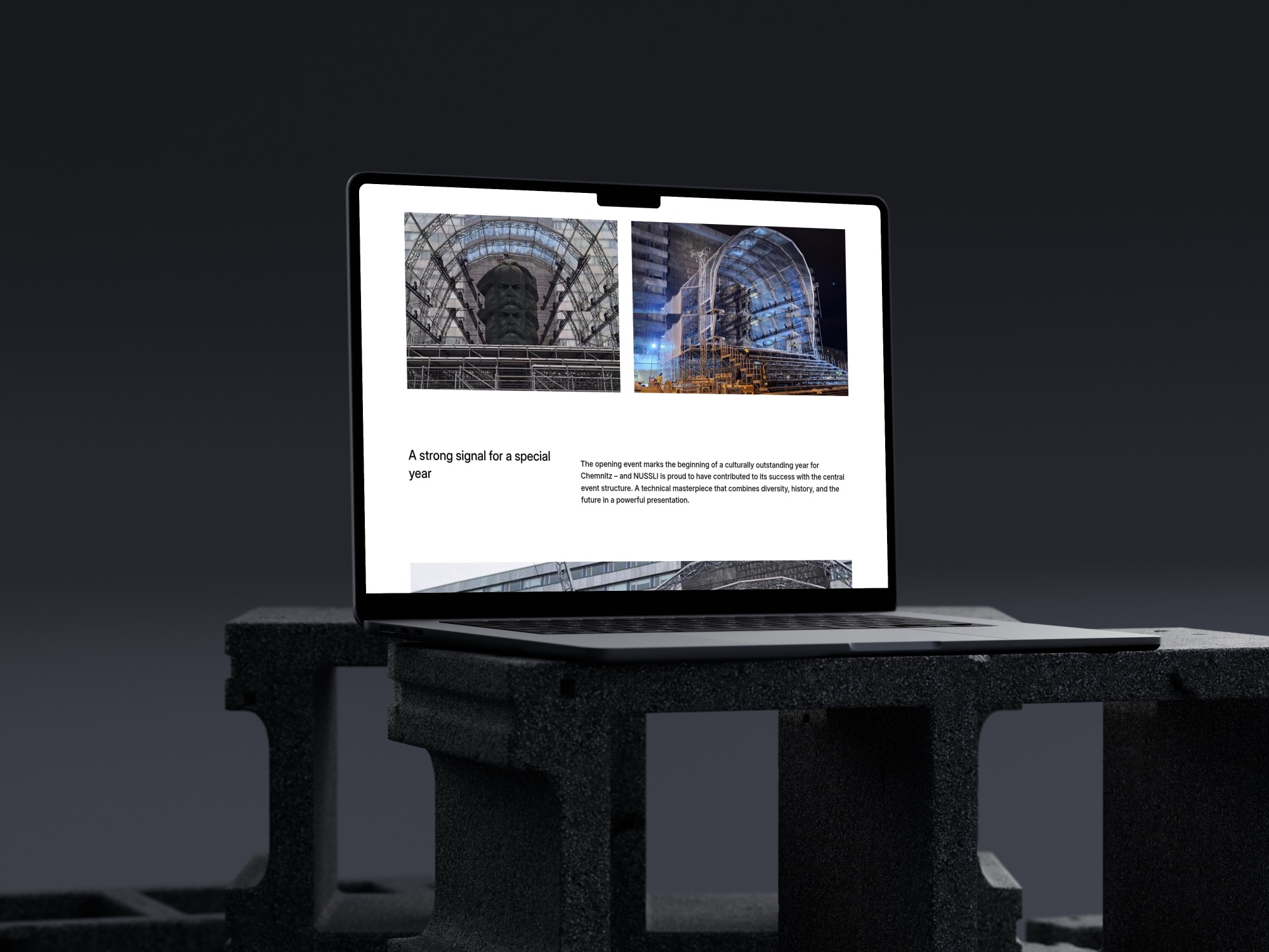Ein Laptop auf einer dunklen Fläche zeigt auf seinem Bildschirm architektonische Bilder und Texte, darunter Fotos von großen, modernen Glasbauten und einen Abschnitt mit der Überschrift Ein starkes Signal für ein besonderes Jahr.