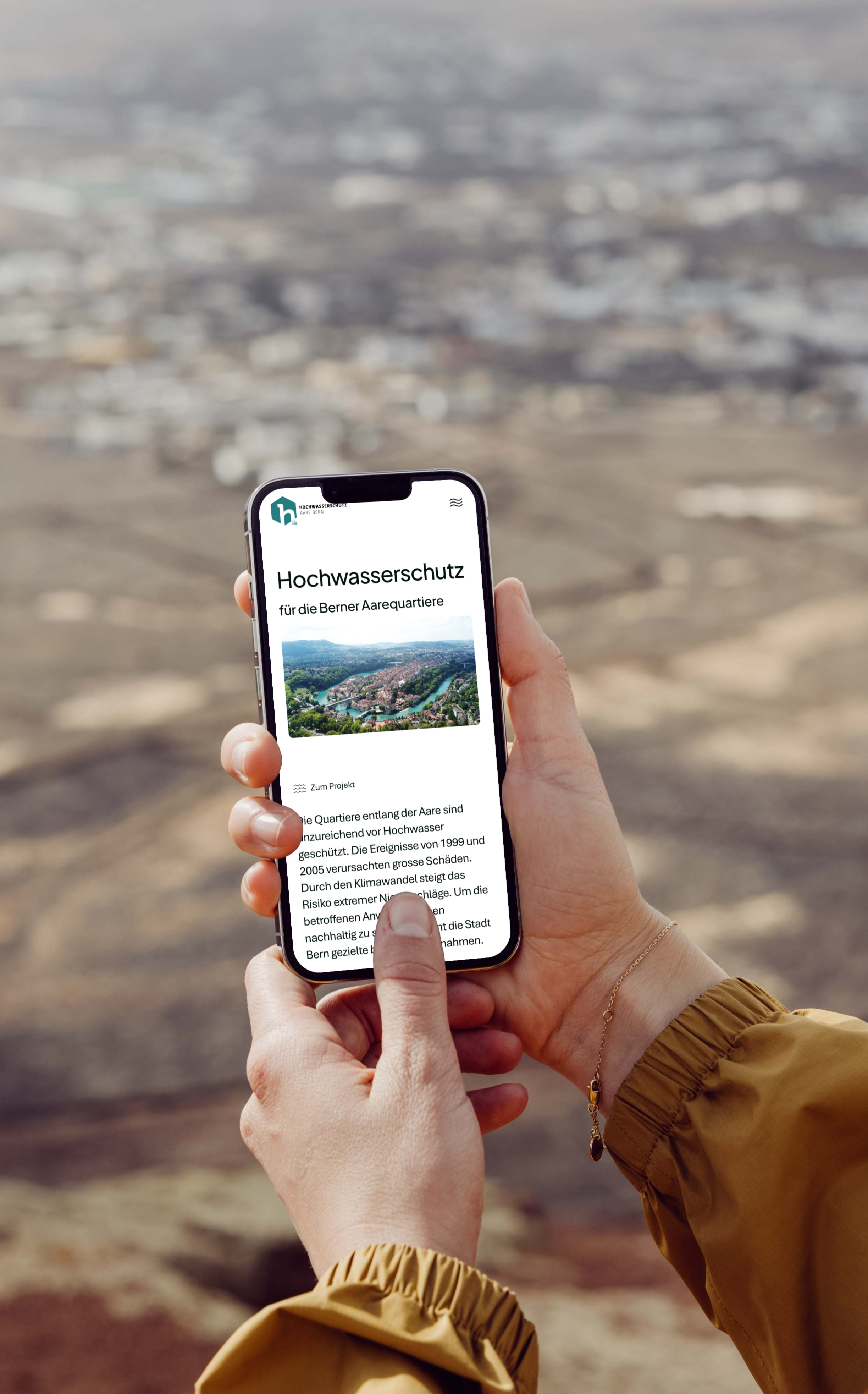 Eine Person, die ein Smartphone in der Hand hält, zeigt eine deutschsprachige Webseite zum Thema Hochwasserschutz an, mit einer unscharfen Außenlandschaft im Hintergrund.