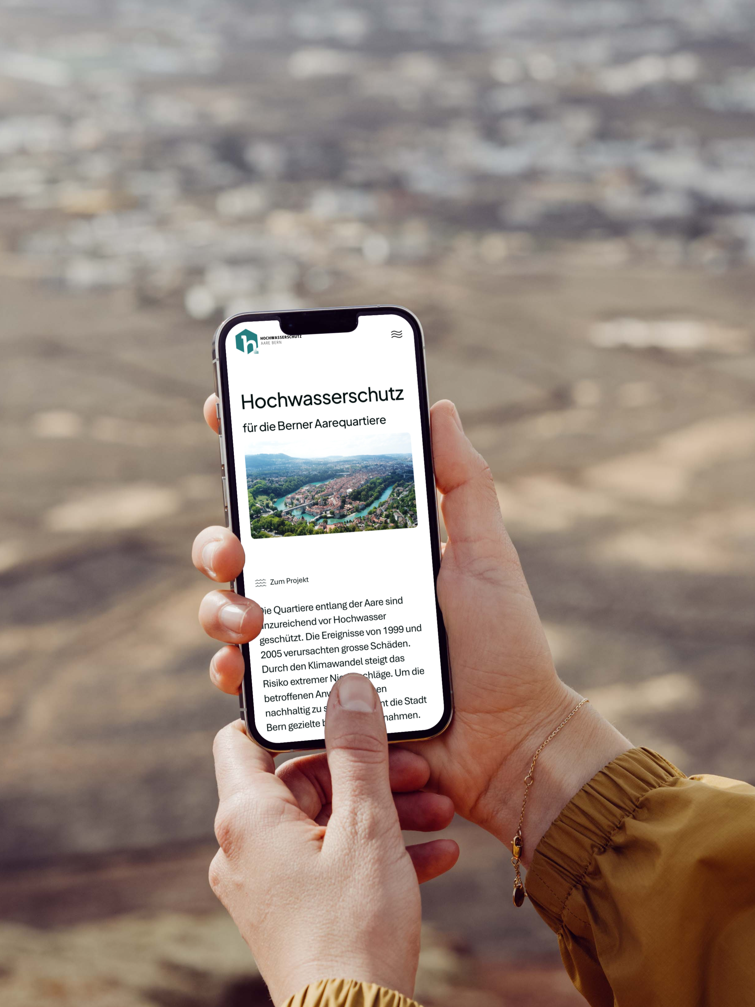 Eine Person, die ein Smartphone in der Hand hält, zeigt eine deutschsprachige Webseite zum Thema Hochwasserschutz an, mit einer unscharfen Außenlandschaft im Hintergrund.