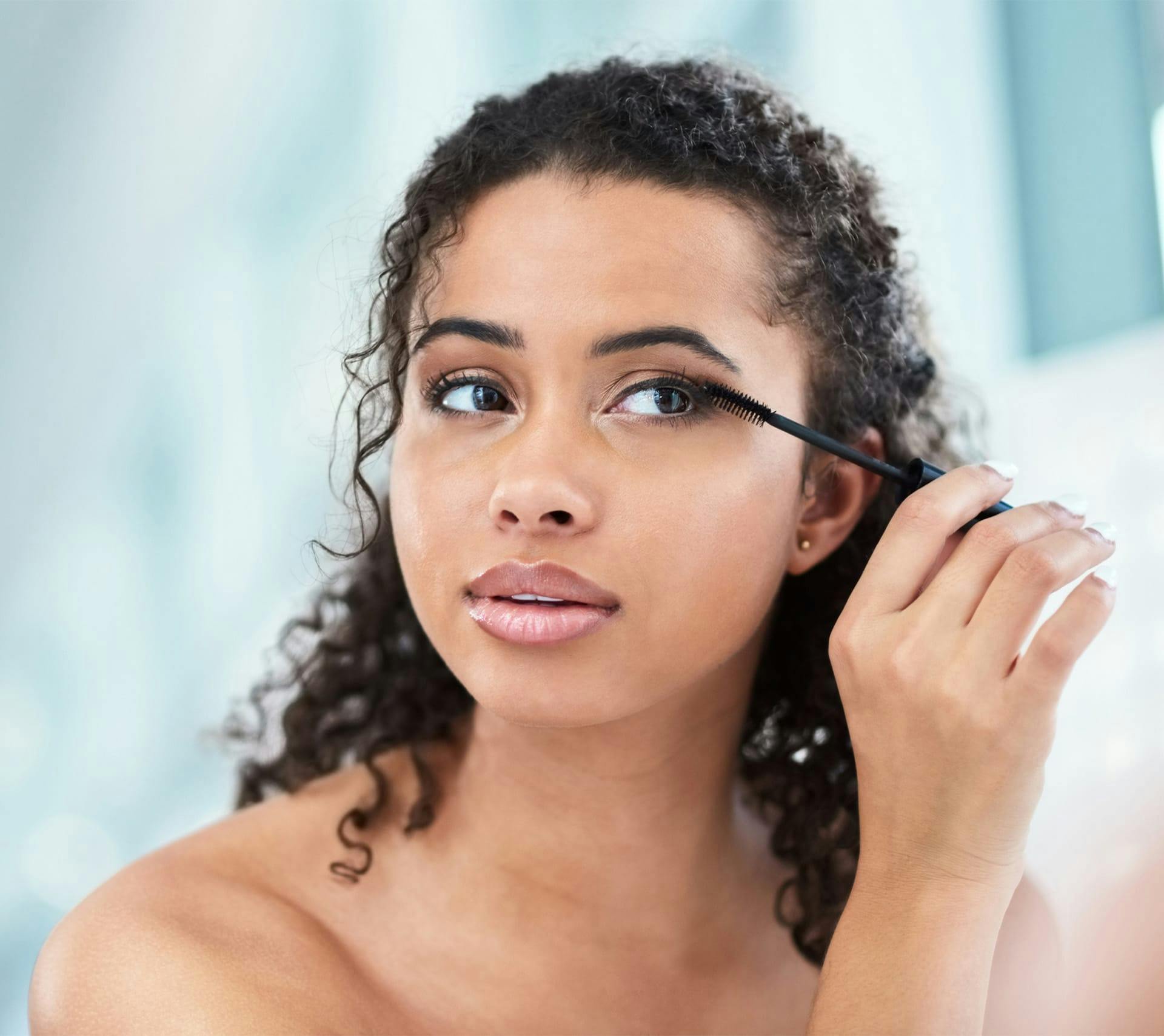 woman with very curly hair putting on mascara