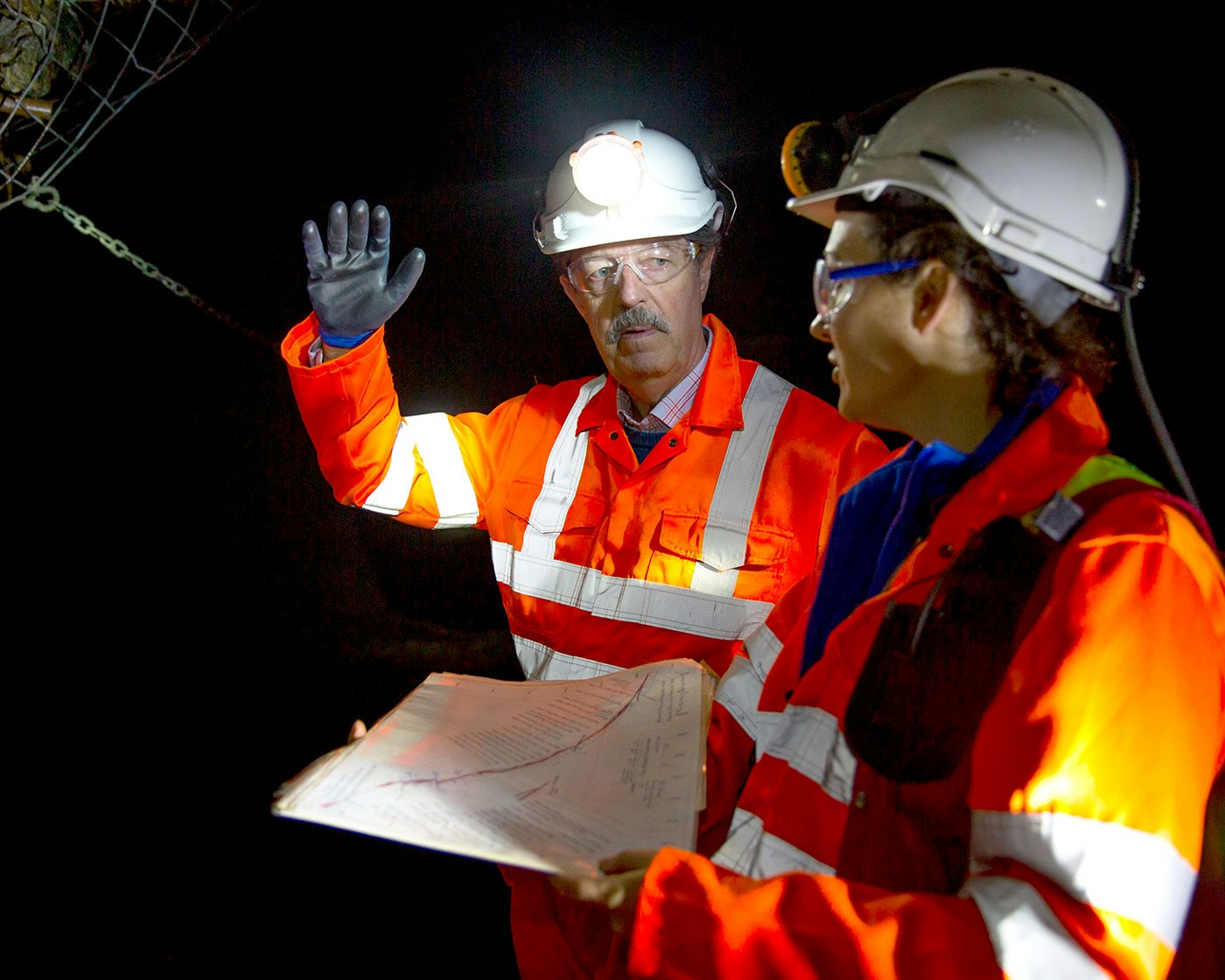 Two people in high vis jackets and hard hats in mine