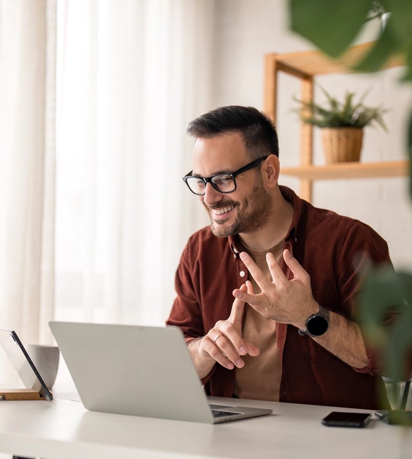 Person working from home, on the computer. He is position at a table, and has a smile.