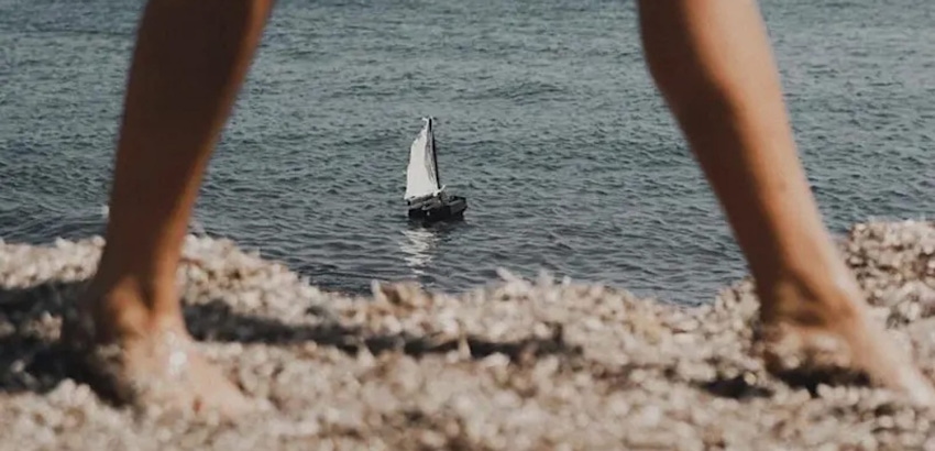 view of a sail boat between persons feet at the beach