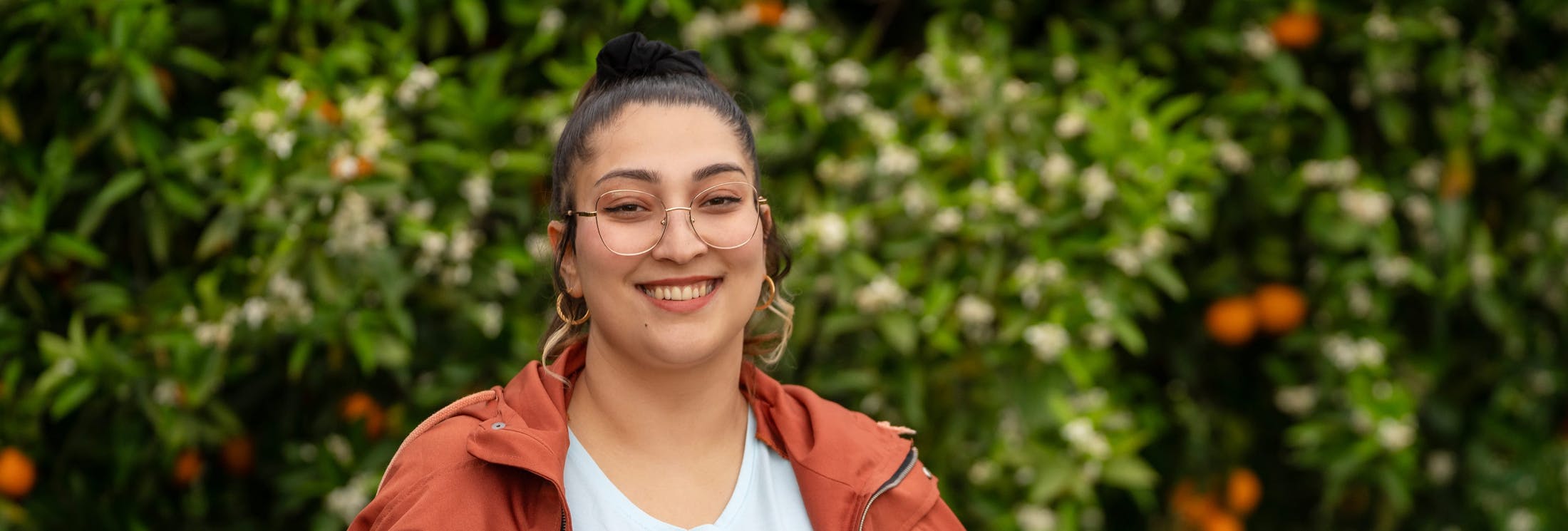 woman in glasses smiling with foliage behind her