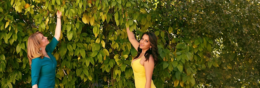 2 ladies in dresses picking fruit from tree