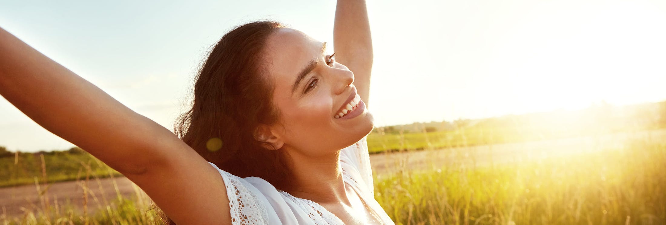 woman with arms up and sunset in background