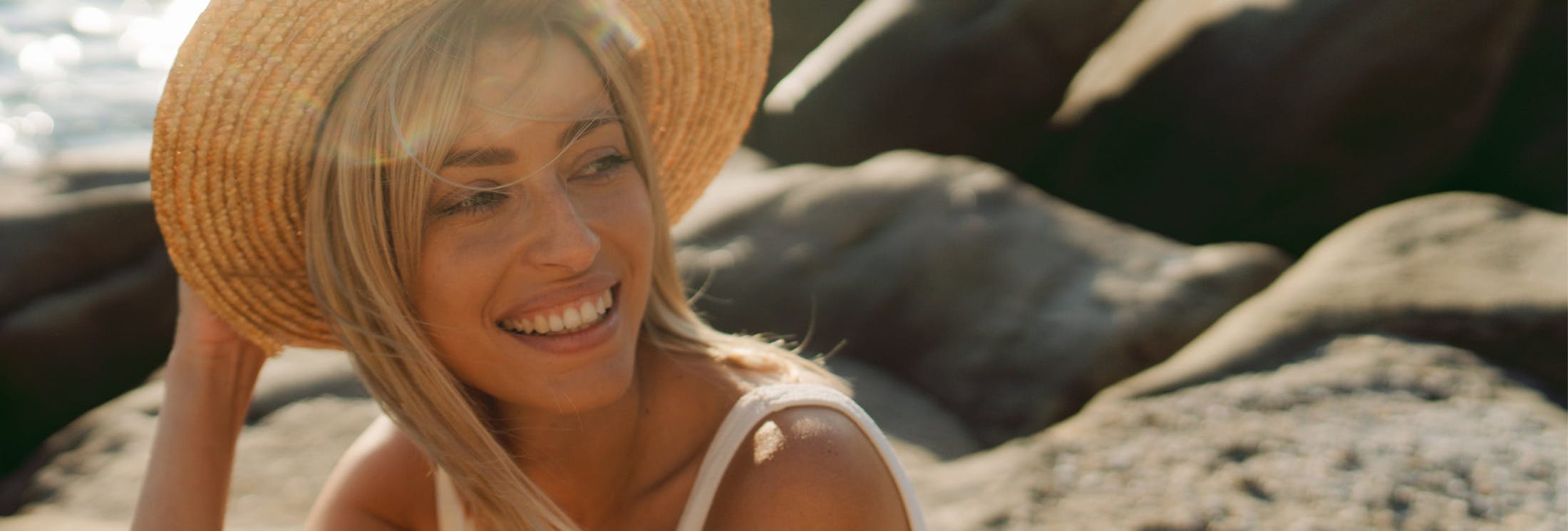 woman in hat sitting on rocks by the beach