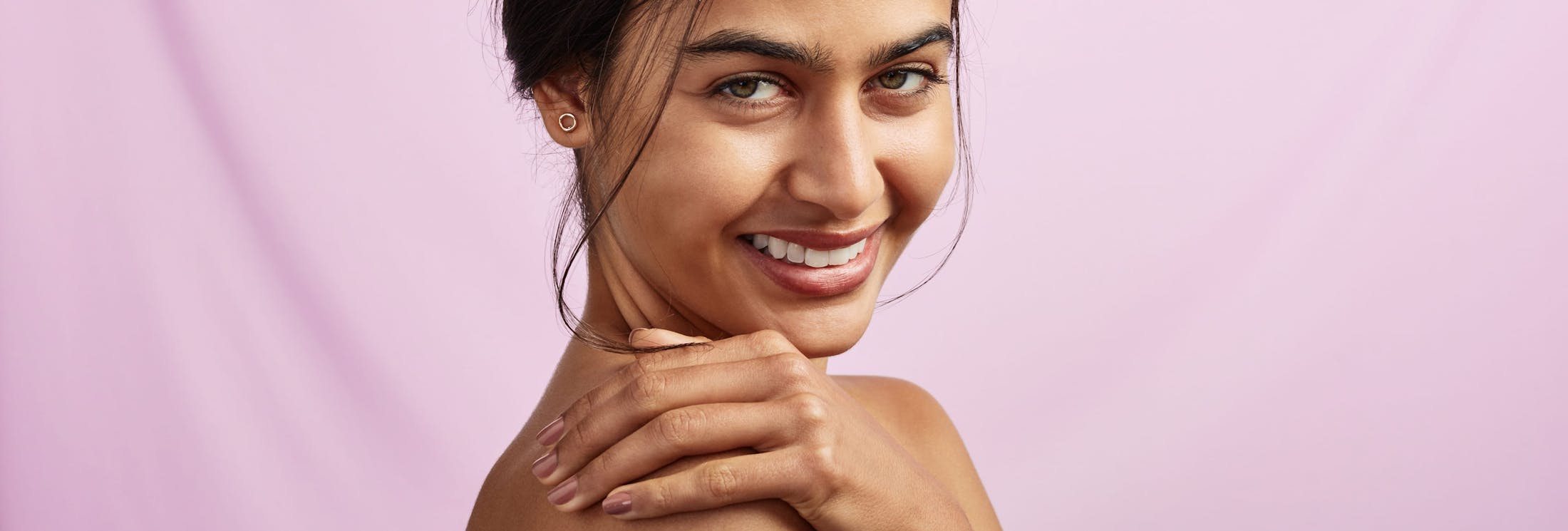woman with hand over shoulder with pink background