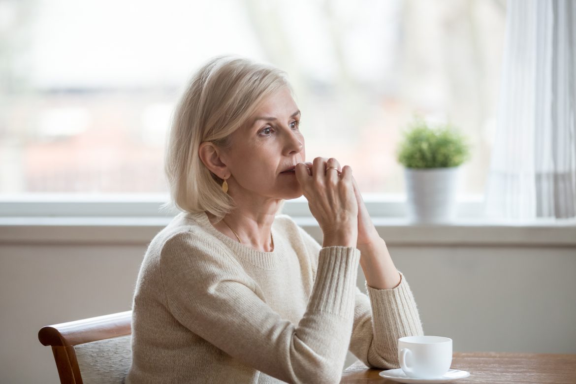 middle aged woman sitting at table drinking tea and thinking