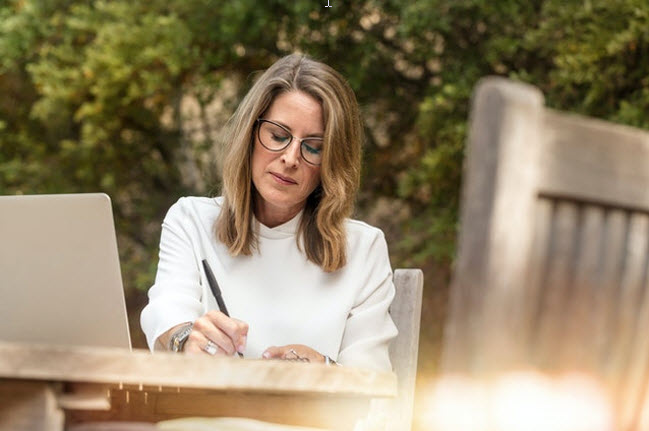 middle aged woman outdoor sitting at table writing 
