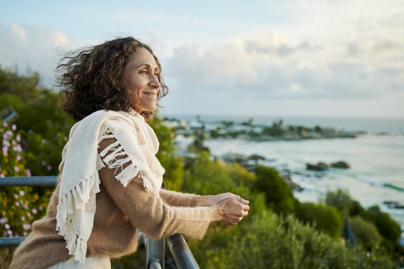 A woman leaning over a rail looking at ocean