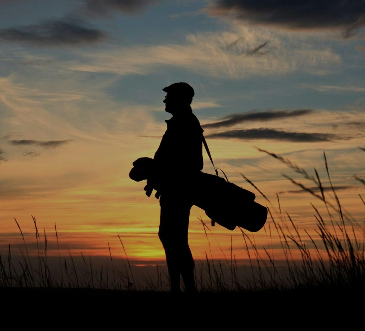 silhouette of a man at sunset, carrying a golf bag