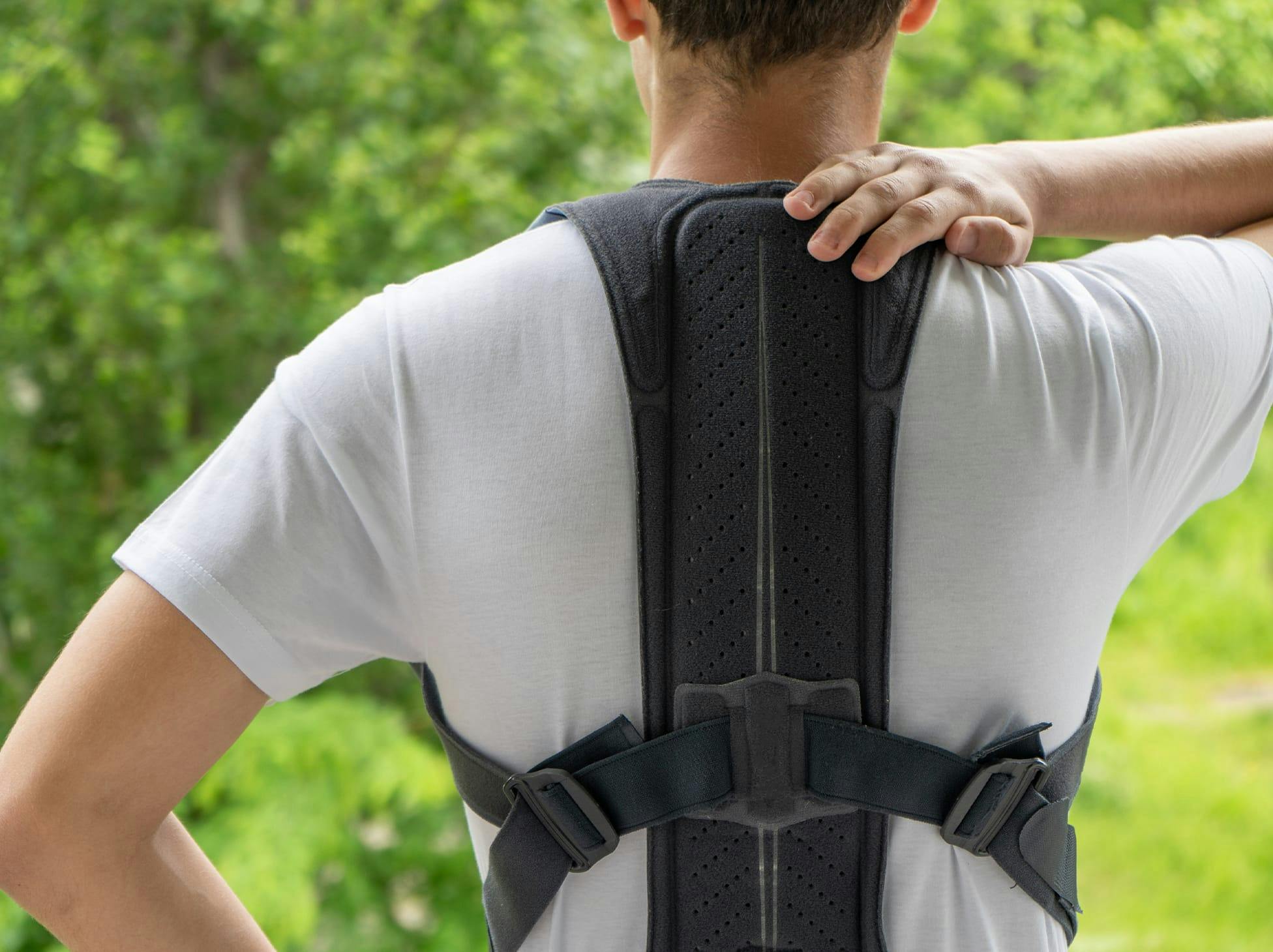 man in a back brace, holding his hand on his shoulder