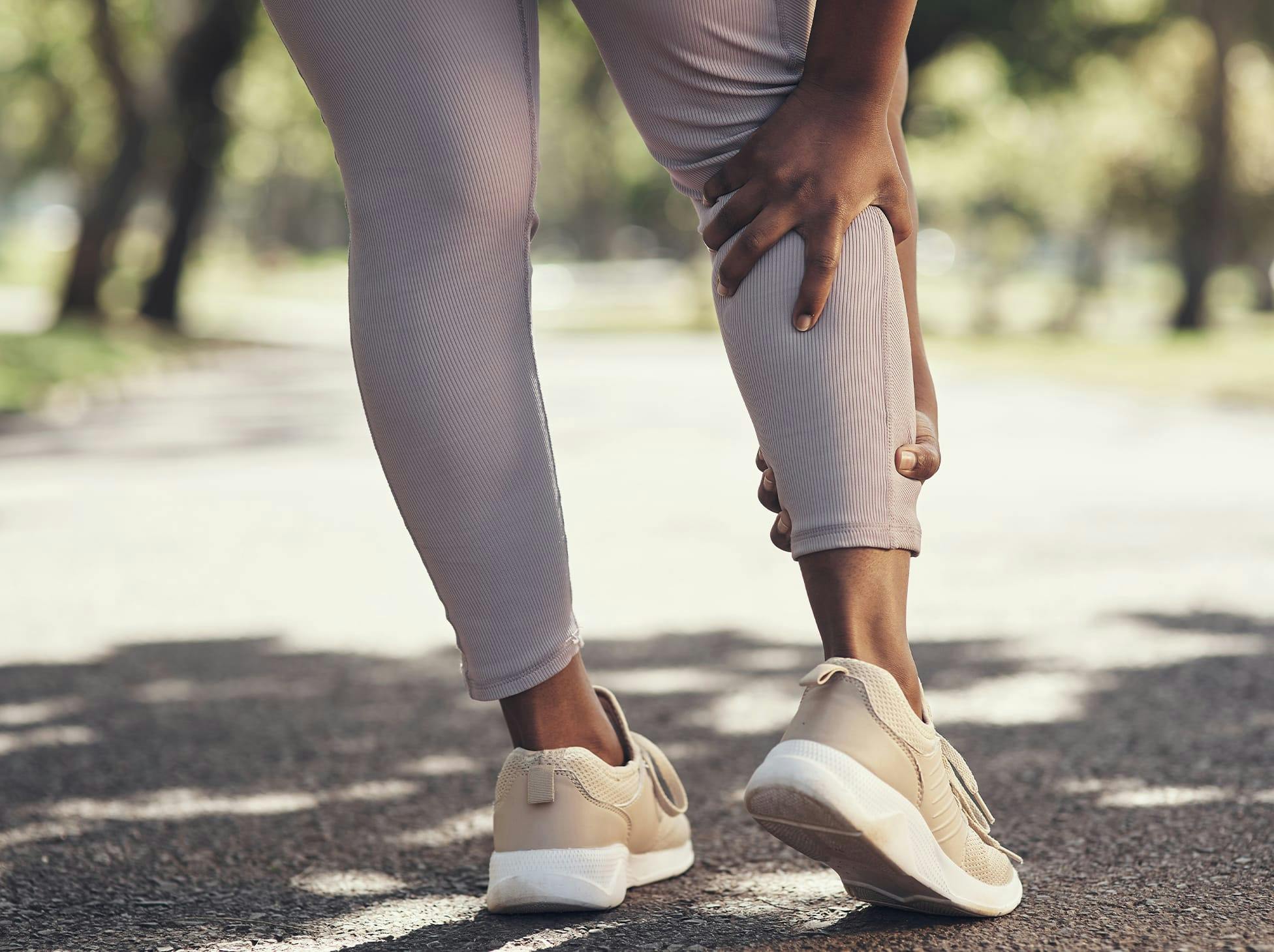 woman holding her lower leg while out exercising