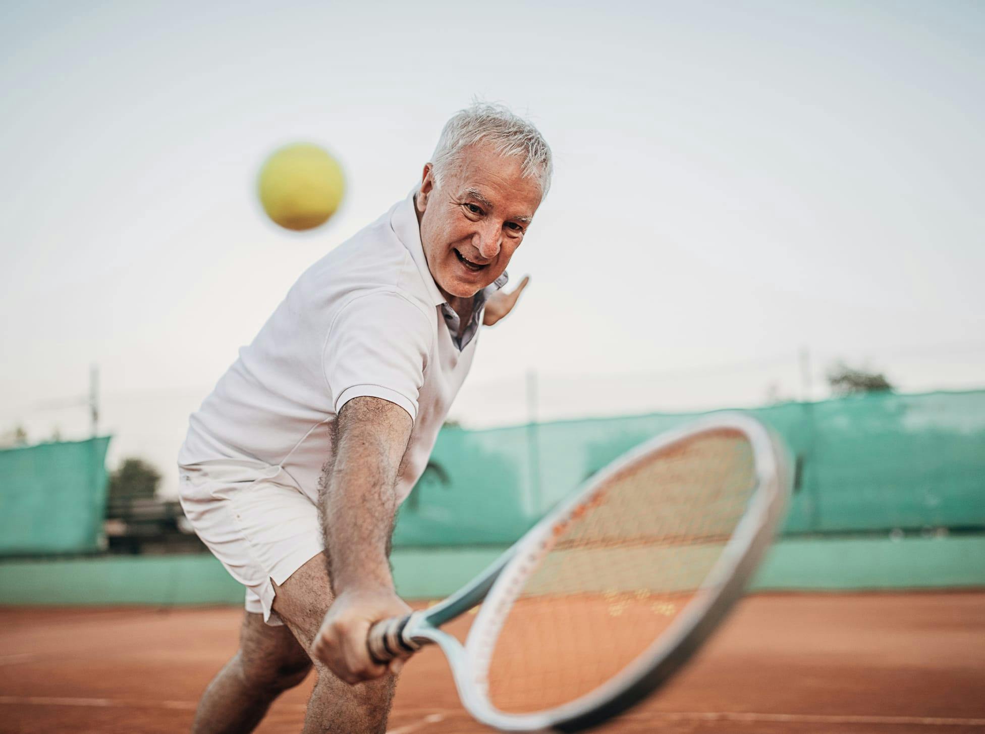 older man hitting a tennis ball with a racket