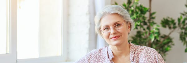 older woman wearing glasses and a pink & white shirt