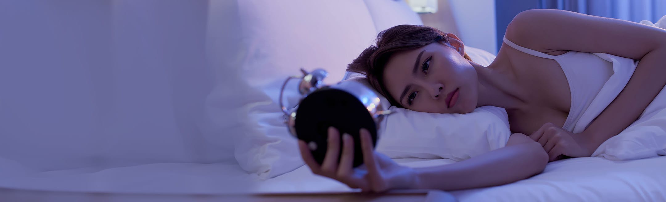 woman laying in bed looking at an alarm clock
