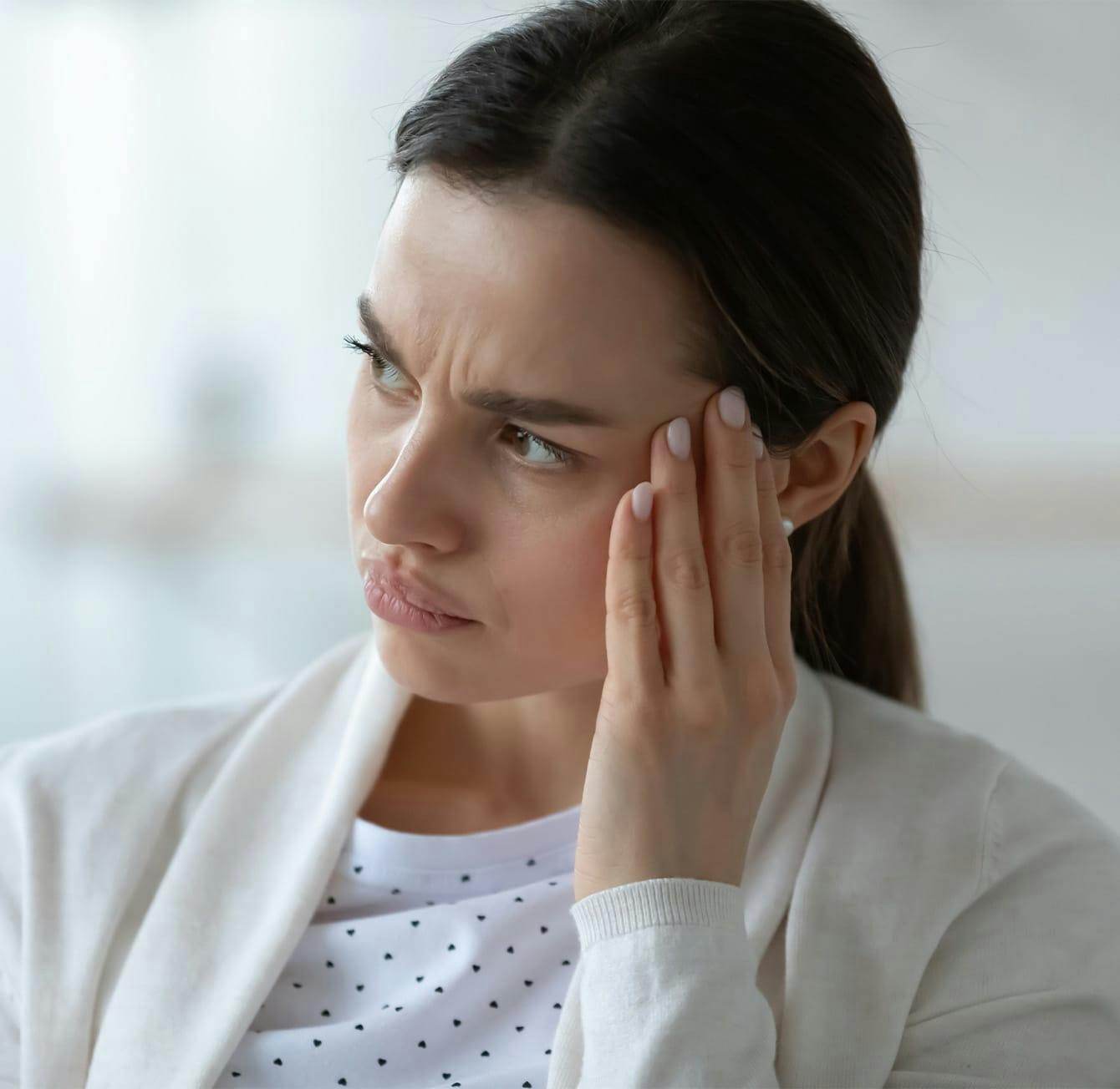 woman touching the side of her face while scrunching her eyebrows