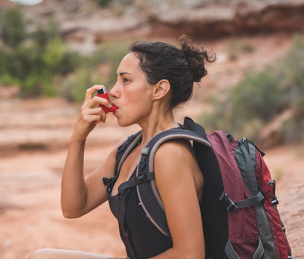 woman using an inhaler while on a hike