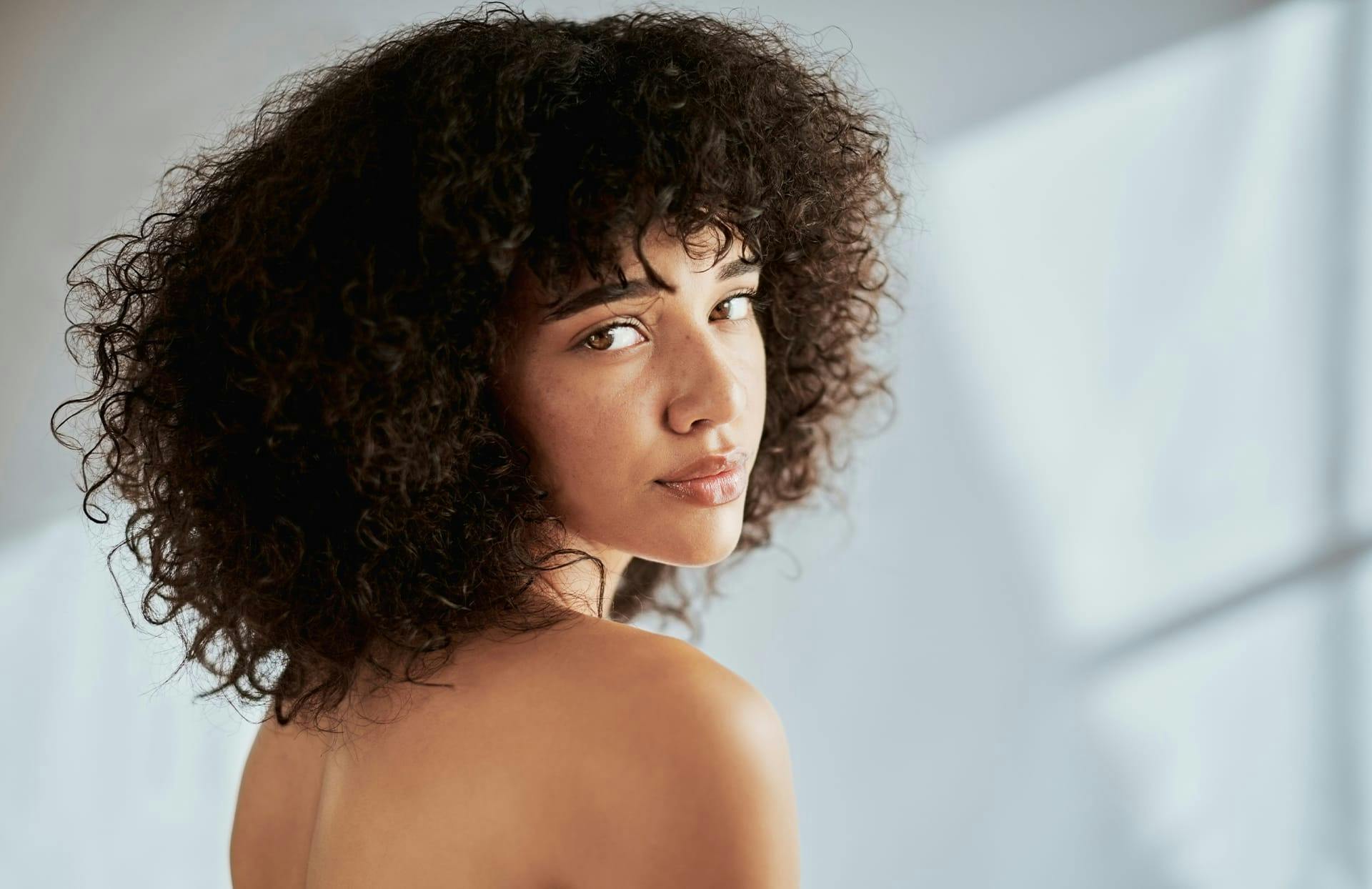 curly-haired woman smiling over shoulder