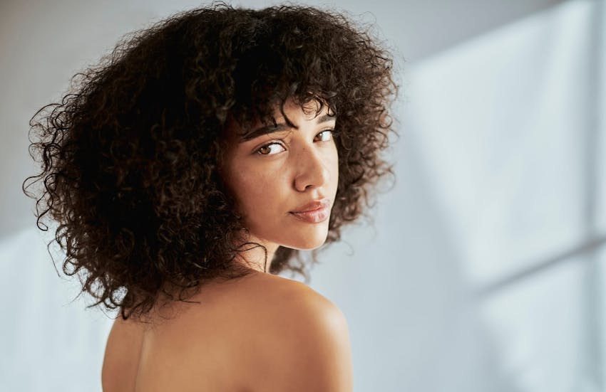curly-haired woman smiling over shoulder