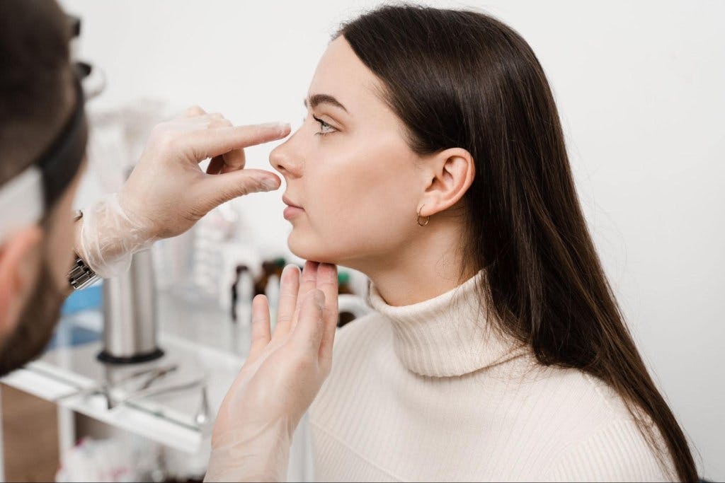 plastic surgeon looking at a female's nose