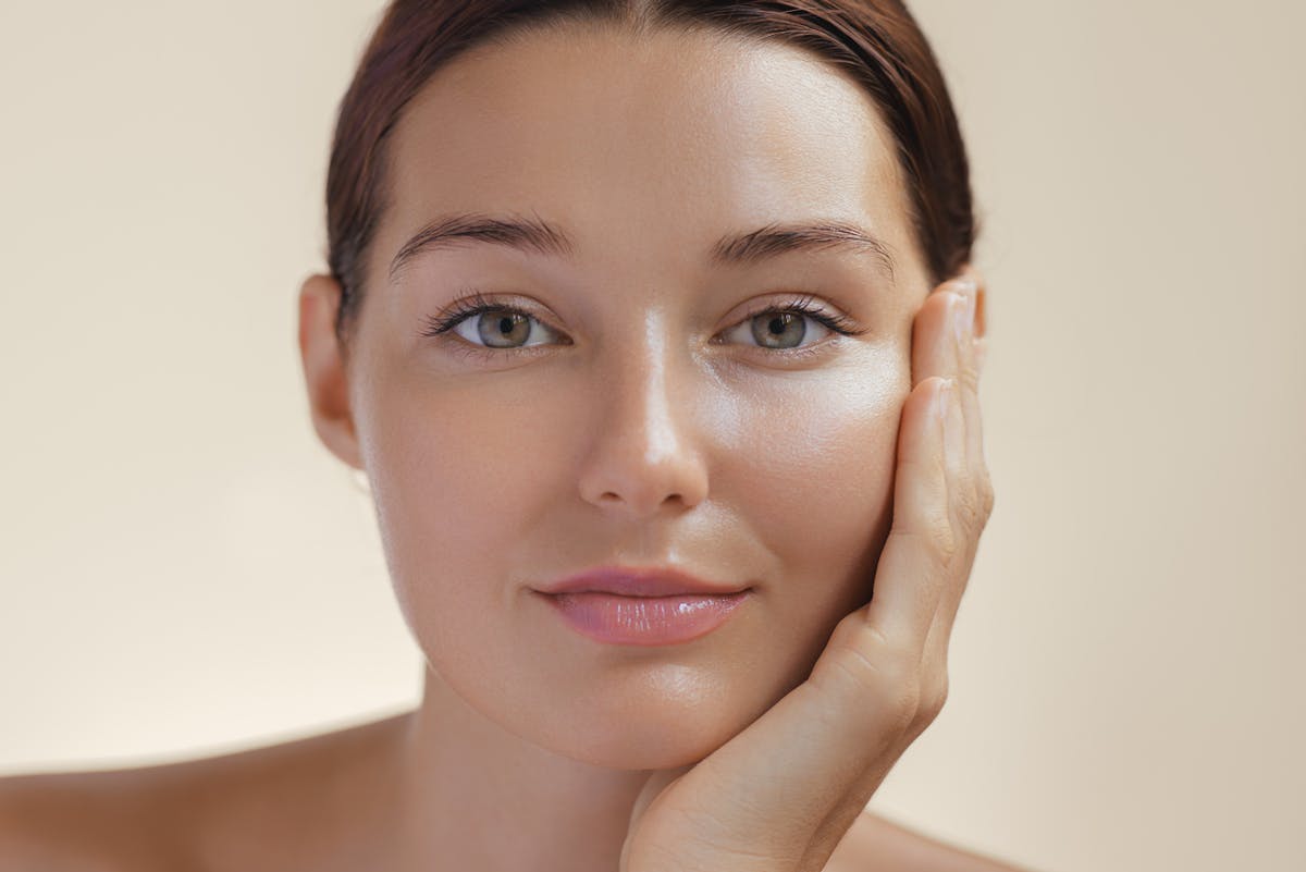 Close-up of a serene young woman with glowing skin resting her face in her hand.
