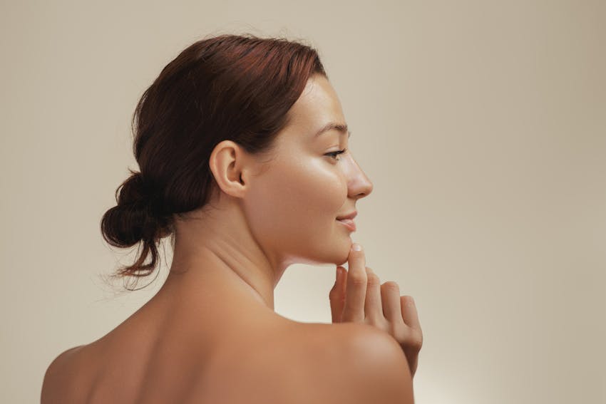Side profile portrait of a young Caucasian woman with glowing, smooth skin, gently touching her chin