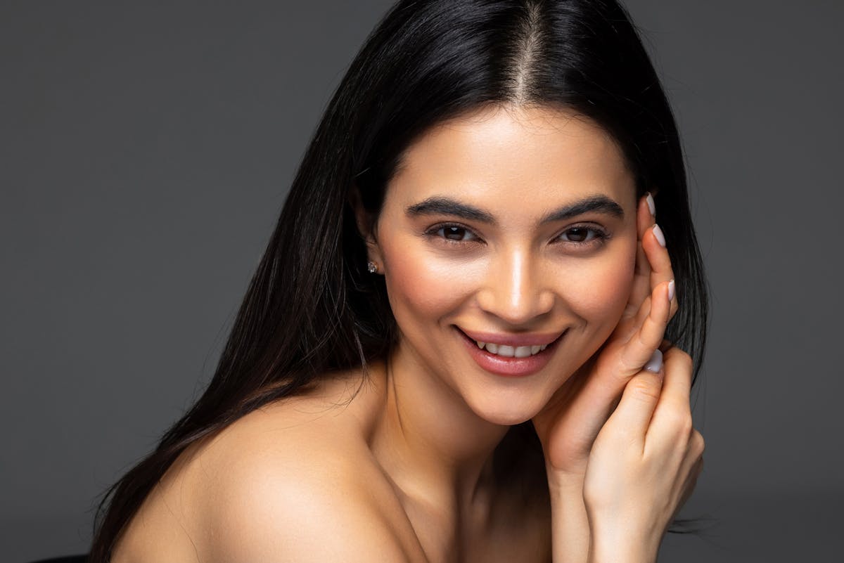 Gorgeous Young Brunette Woman face portrait. Beauty Model Girl with bright eyebrows, perfect make-up, red lips, touching her face